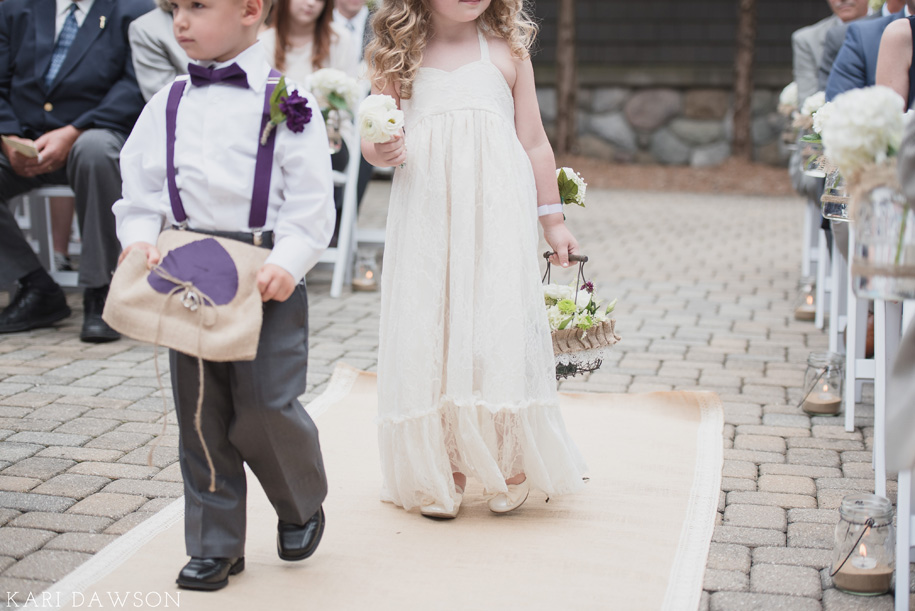 Ring bearer and flower girl walk down the aisle on a burlap runner for this rustic elegant outdoor wedding ceremony in the woods 
