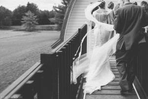 Cathedral length wedding veil caught in the wind and her lace mermaid style wedding dress with off the should cap sleeves and sheer back with buttons by Kari Dawson Photography