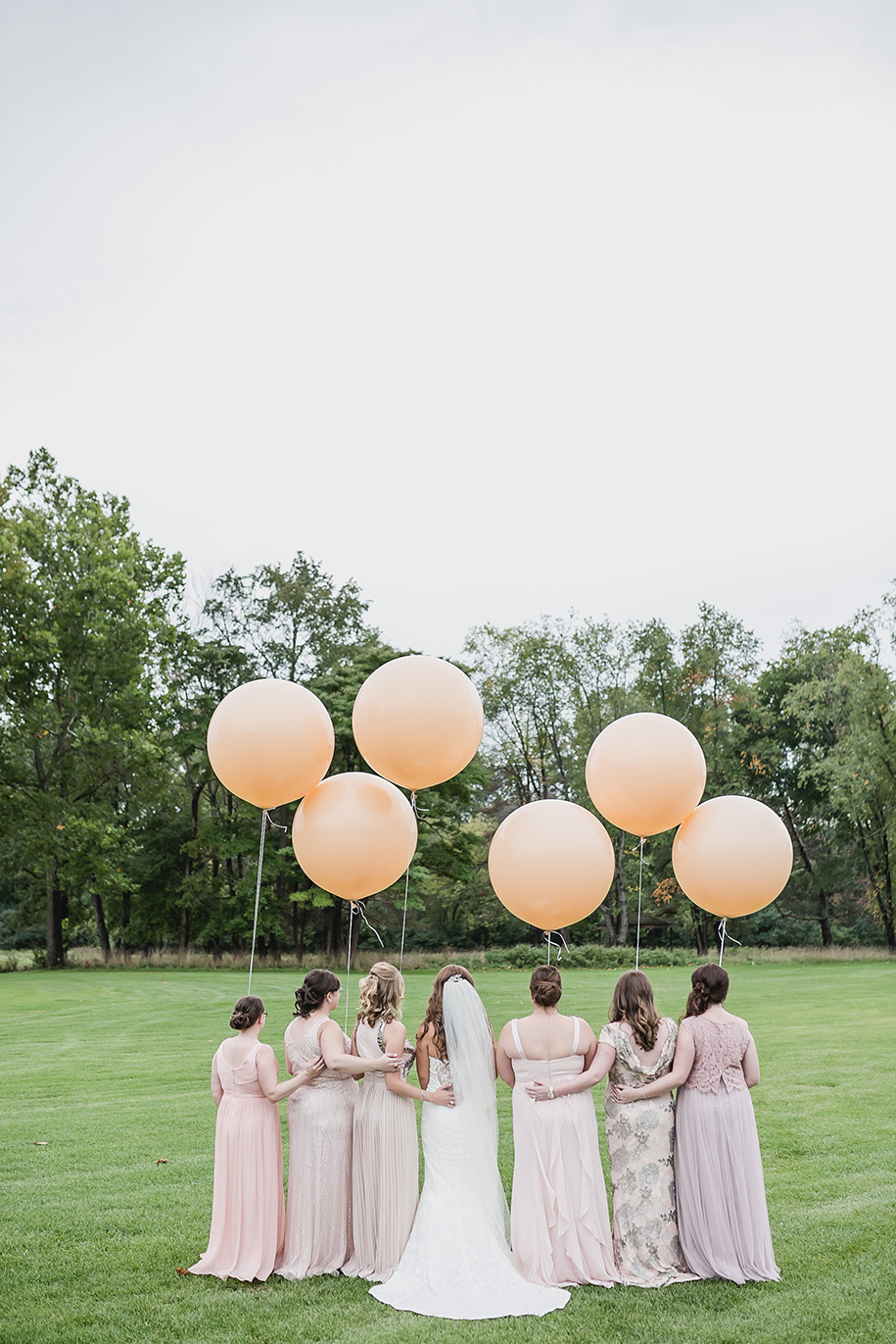 Bridesmaids in blush with giant balloons! The bride wore a sweetheart shaped strapless dress with a fitted bodice, lace overlay and short train without a bustle. The bridesmaids each chose their own dress in various shades of blush and sequins.