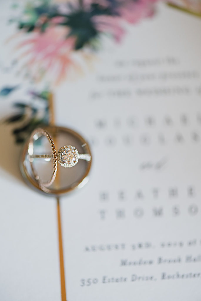 Gorgeous halo solitaire diamond engagement ring and rope gold wedding band set atop her whimsical wedding invitation suite. Colorful Meadow Brook Mansion wedding in Rochester, Michigan provided by Kari Dawson, top-rated Rochester, Michigan wedding photographer, and her team. 