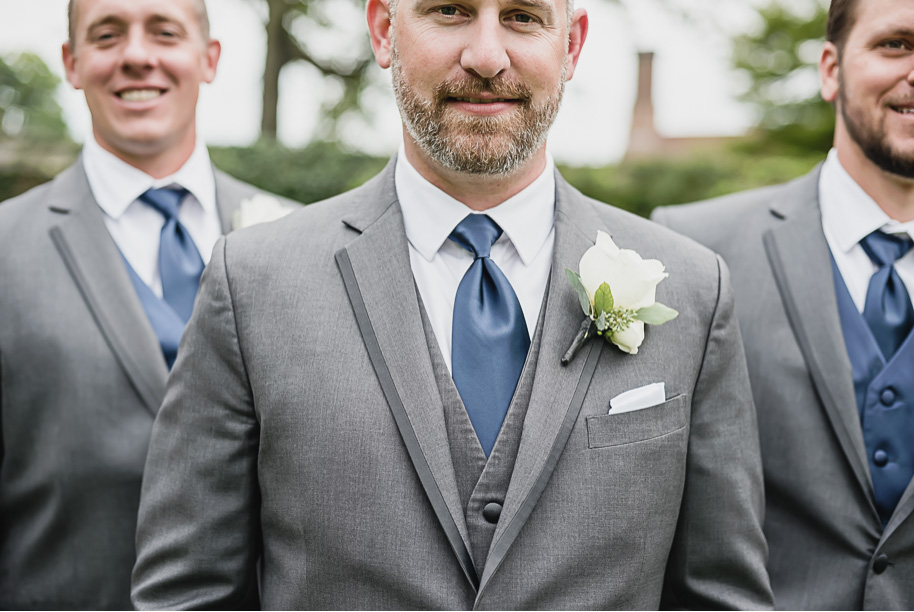 Gray Mens Wearhouse suits paired with navy neck ties and cream rose boutonnieres. Gray and navy Meadow Brook wedding at Meadow Brook Hall and Gardens in Rochester, Michigan provided by Kari Dawson, top-rated Rochester engagement and wedding photographer, and her team. 