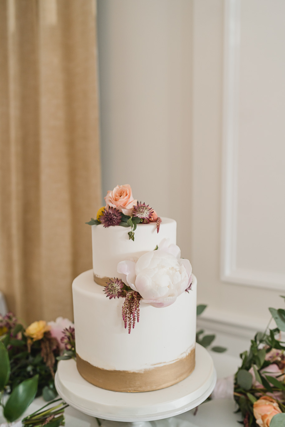 Two layer cream and gold wedding day cake with peonies. An intimate destination Mackinac Island wedding at Mission Point Resort with a cranberry and black color palette provided by Kari Dawson, top-rated Northern Michigan wedding photographer, and her team.