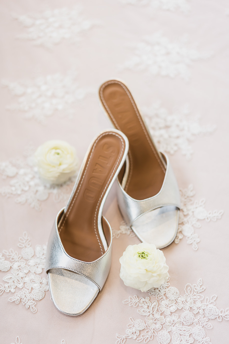 Silver bridal heels styled with white ranunculus on lace fabric before the Bay Pointe Jewish wedding celebration.