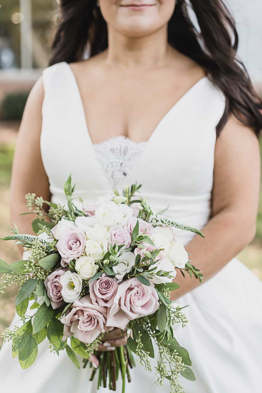A romantic bouquet featuring blush and ivory roses, lisianthus, and lush greenery carried by the bride in her timeless white gown.