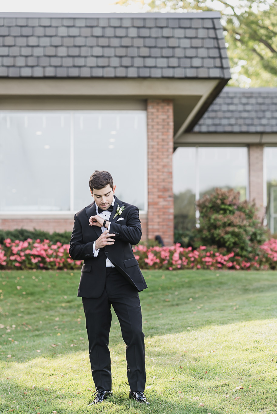A close-up of the groom adjusting his cufflinks, showcasing his sharp black tuxedo, boutonniere, and luxury watch.