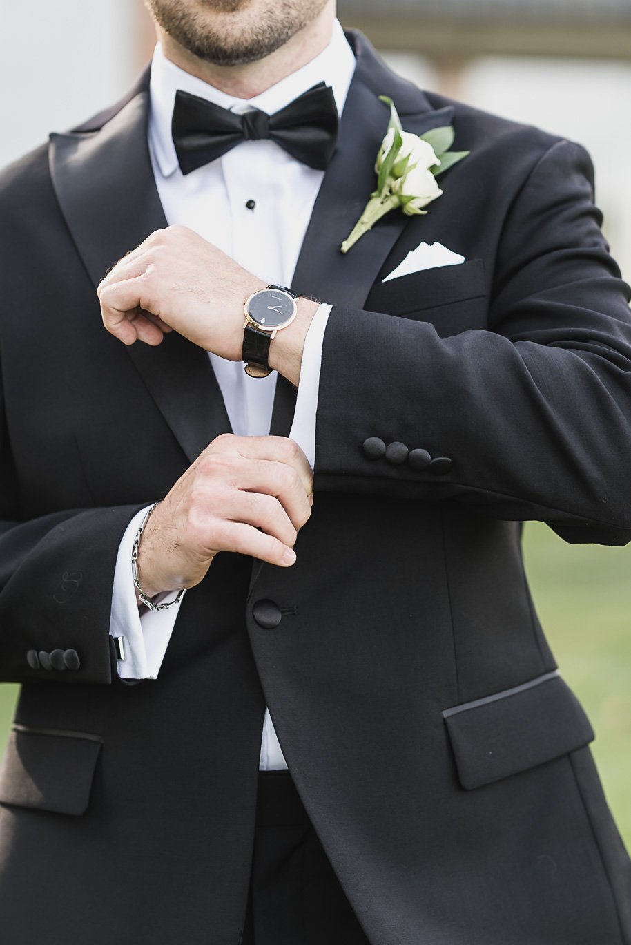 A close-up of the groom adjusting his cufflinks, showcasing his sharp black tuxedo, boutonniere, and luxury watch.