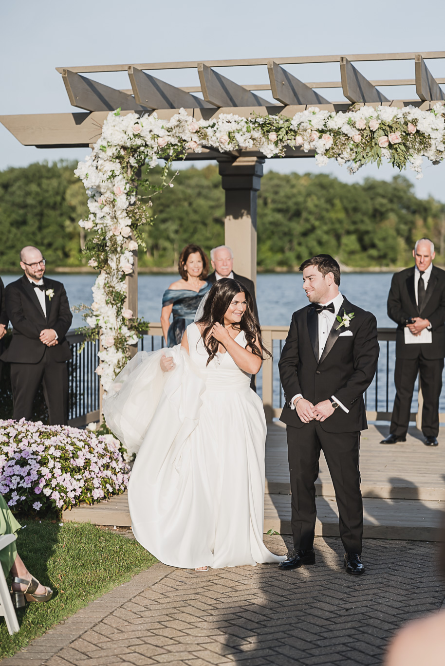 Bride and groom share a joyful glance under a flower-covered chuppah at their waterfront Bay Pointe Golf Club wedding ceremony.