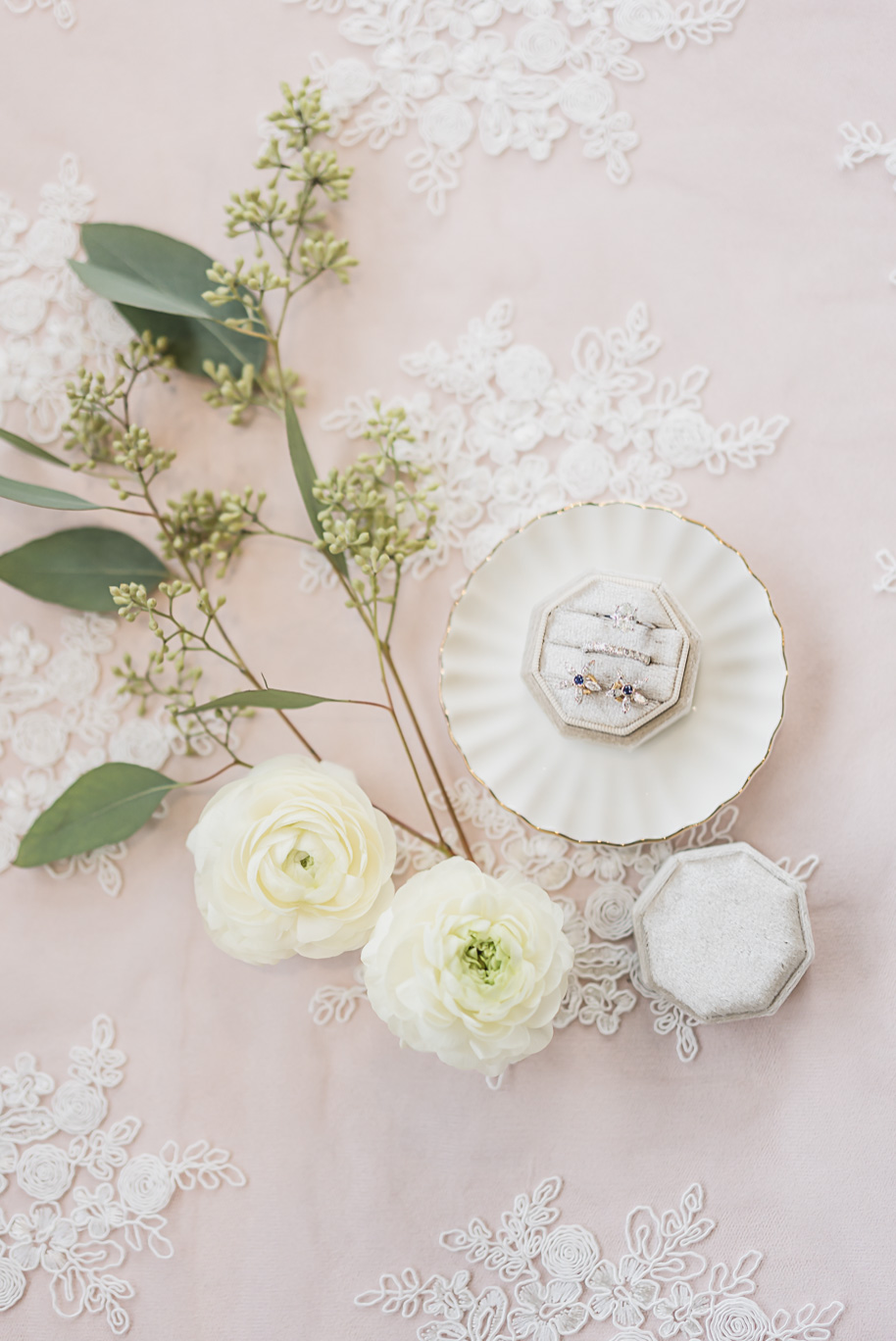 Diamond wedding rings displayed in velvet boxes with white florals on blush lace, photographed at Bay Pointe Jewish wedding.
