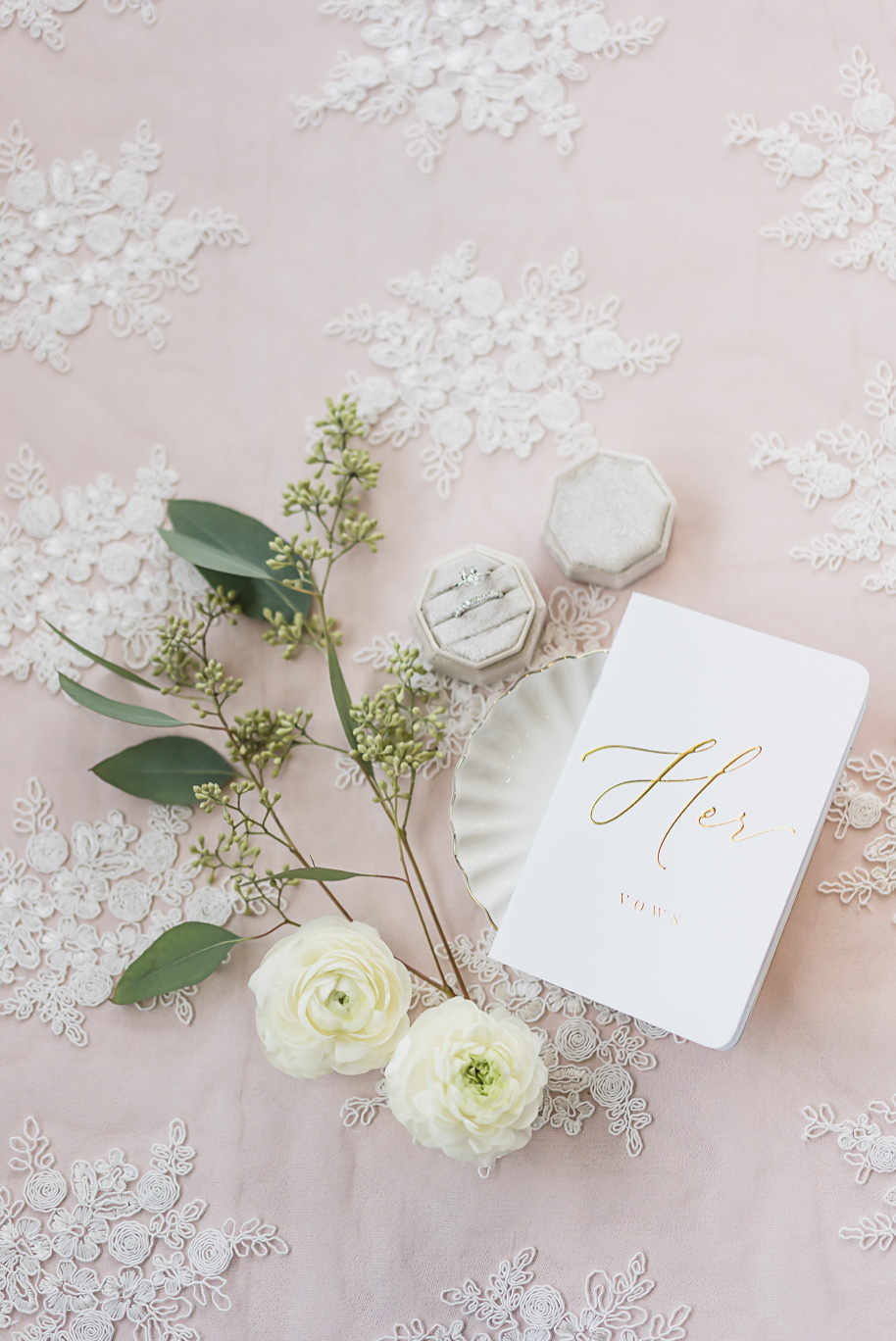 “Her Vows” book styled with diamond rings and fresh white florals on pink lace for Bay Pointe Jewish wedding details.
