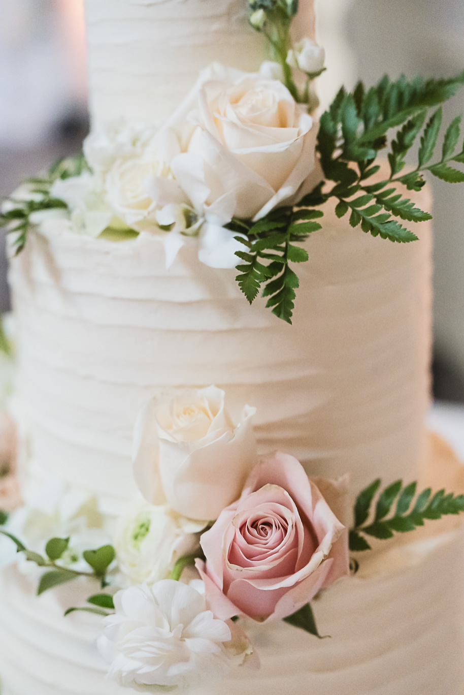 Elegant white wedding cake decorated with fresh blush pink and ivory roses with greenery, photographed at Bay Pointe Golf Club wedding reception.