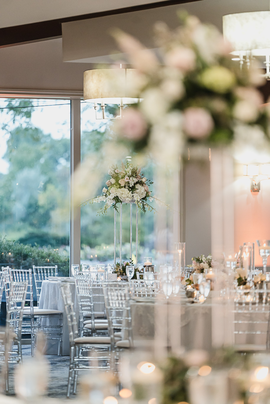 Romantic Bay Pointe Golf Club reception with tall floral centerpieces, soft candlelight, and clear chiavari chairs creating an elegant ballroom atmosphere.