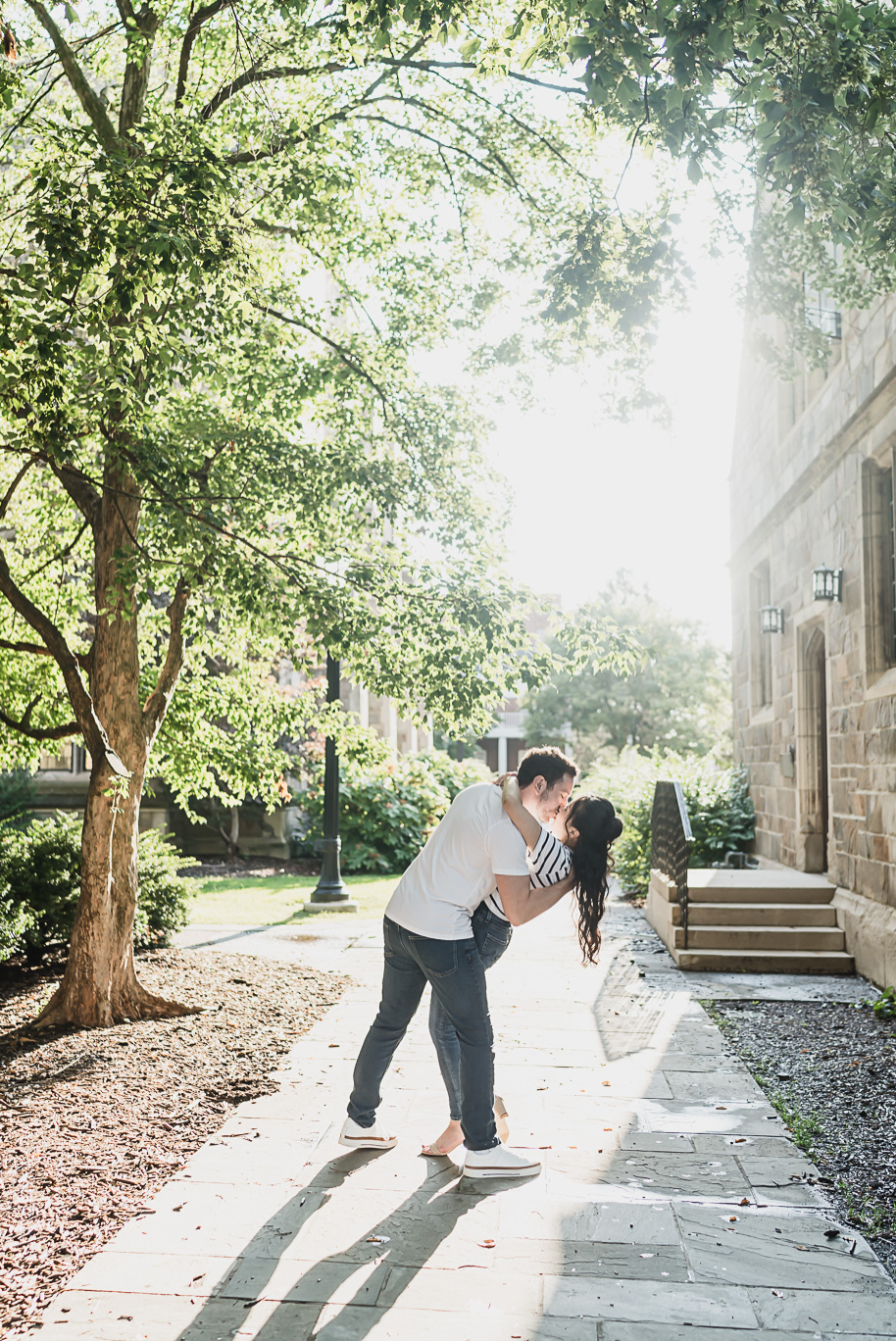 Playful dip kiss beneath glowing summer sunlight at the University of Michigan Law Quad, a romantic engagement photo full of joy and elegance.