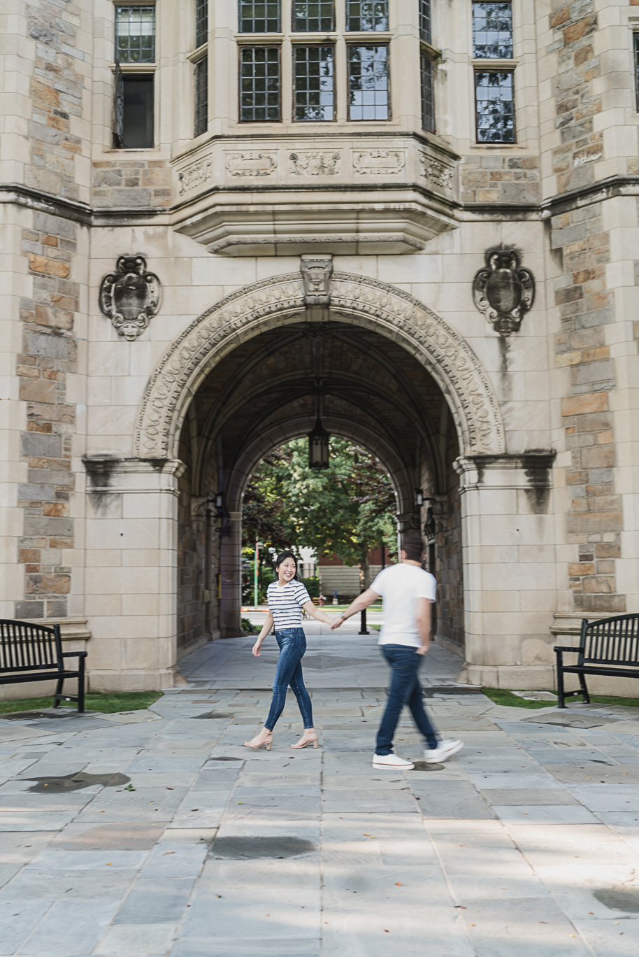 Couple holding hands while walking through the historic stone archways of Michigan Law Quad, blending romance with the timeless architecture of Ann Arbor.