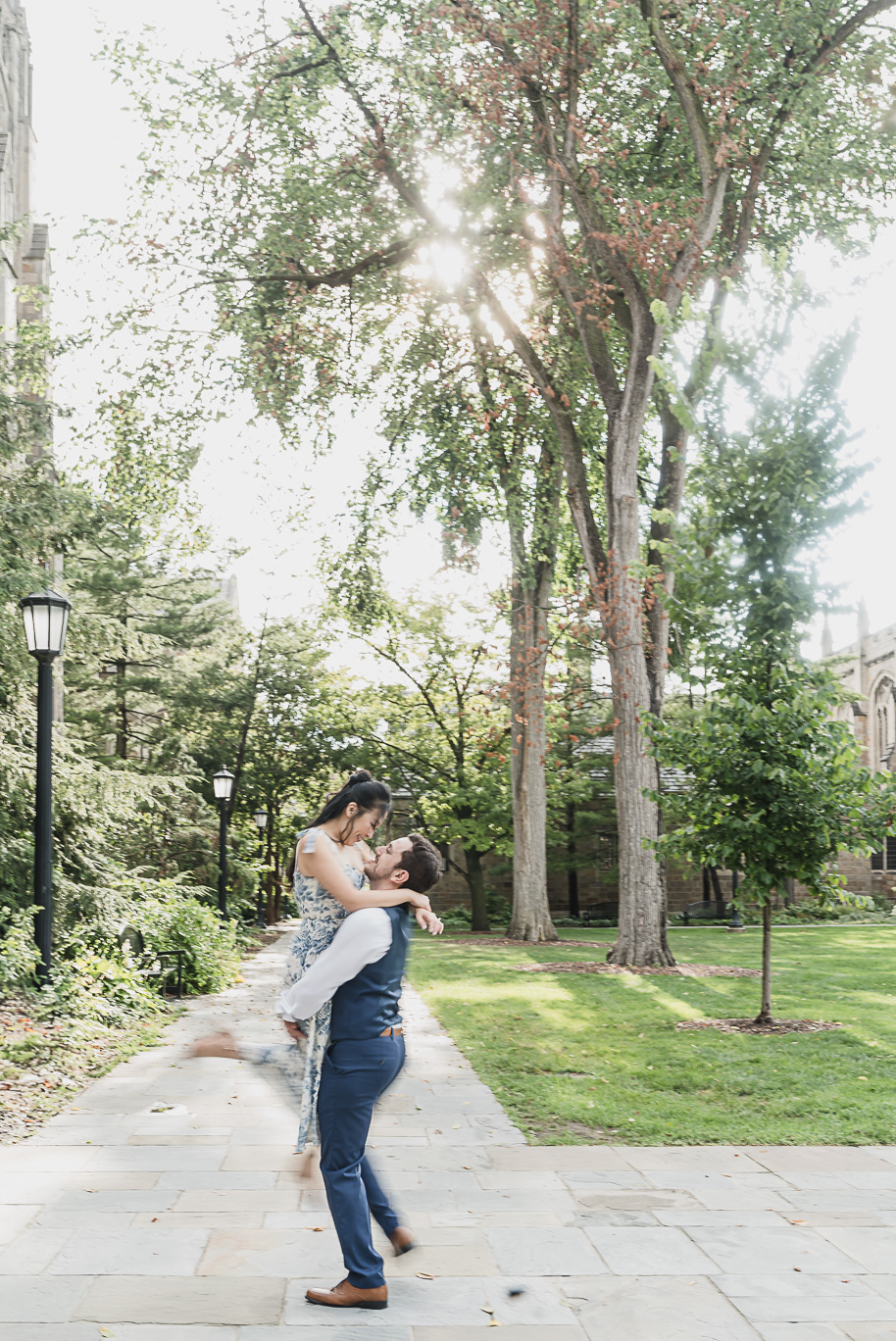 Playful moment at a Michigan Law Quad engagement as Alex lifts Linda under the sunlit trees, blending romance and joy in this iconic Ann Arbor setting.