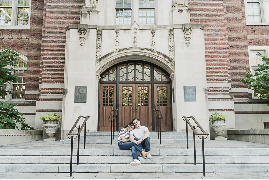Wide shot of engaged couple sitting together on the grand stone steps at the University of Michigan Law Quad, perfect for couples seeking classic and romantic engagement photos.