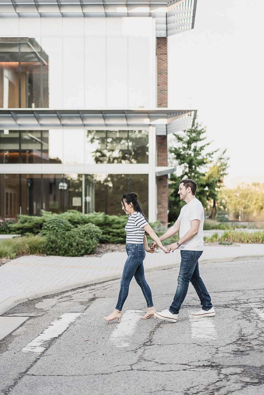 Couple walking hand in hand across a crosswalk on campus, editorial detail from their Michigan Law Quad engagement session.