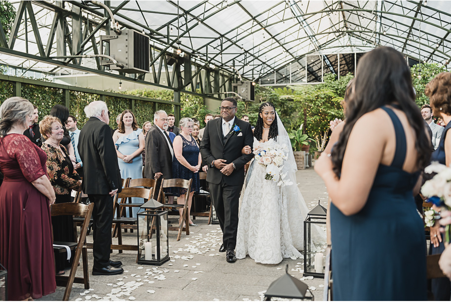 An elegant fall Planterra Conservatory wedding captured by Kari Dawson + Co in Bloomfield Hills, Michigan. This Euro-inspired greenhouse celebration featured lush floral design, golden candlelight, and heartfelt vows beneath the glass canopy. Perfect inspiration for couples dreaming of a romantic Michigan wedding surrounded by nature and timeless architecture.
