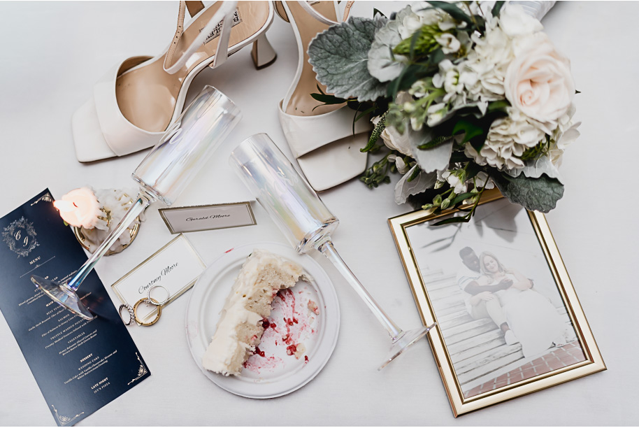 Elegant flat-lay of wedding day details from a Castle Farms wedding in Northern Michigan. Captured by Kari Dawson + Co, featuring bridal heels, bouquet, champagne flutes, vows, and a framed engagement photo styled with timeless florals and romantic neutral tones.