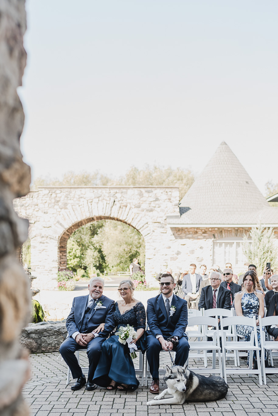 “Wedding guests seated outdoors at Castle Farms in Charlevoix, Michigan with the couple’s dog resting at their feet. Captured by Kari Dawson + Co, this elegant pre-ceremony moment highlights emotional connection and timeless outdoor wedding style.