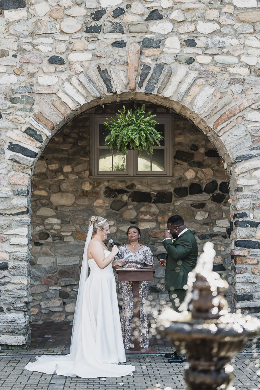 Bride and groom share an elegant moment in front of the stone archway at Castle Farms in Charlevoix, Northern Michigan. Captured by Kari Dawson + Co, this editorial portrait highlights timeless black-tie wedding style in green and gold.