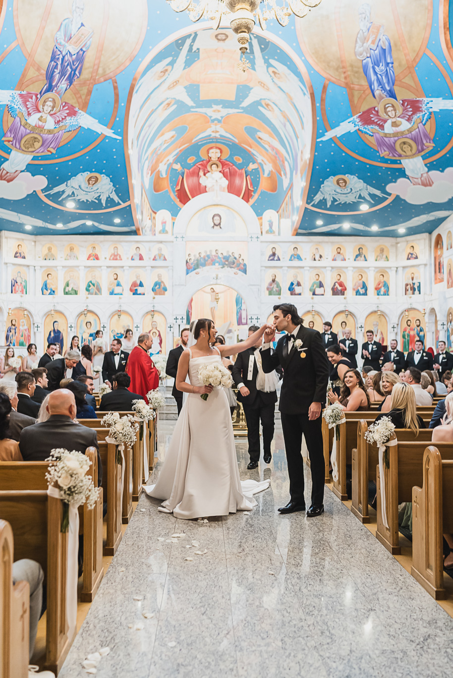 Bride and groom share a kiss during their Macedonian wedding ceremony inside Nativity of the Virgin Mary, surrounded by vibrant domed ceilings and biblical murals.
