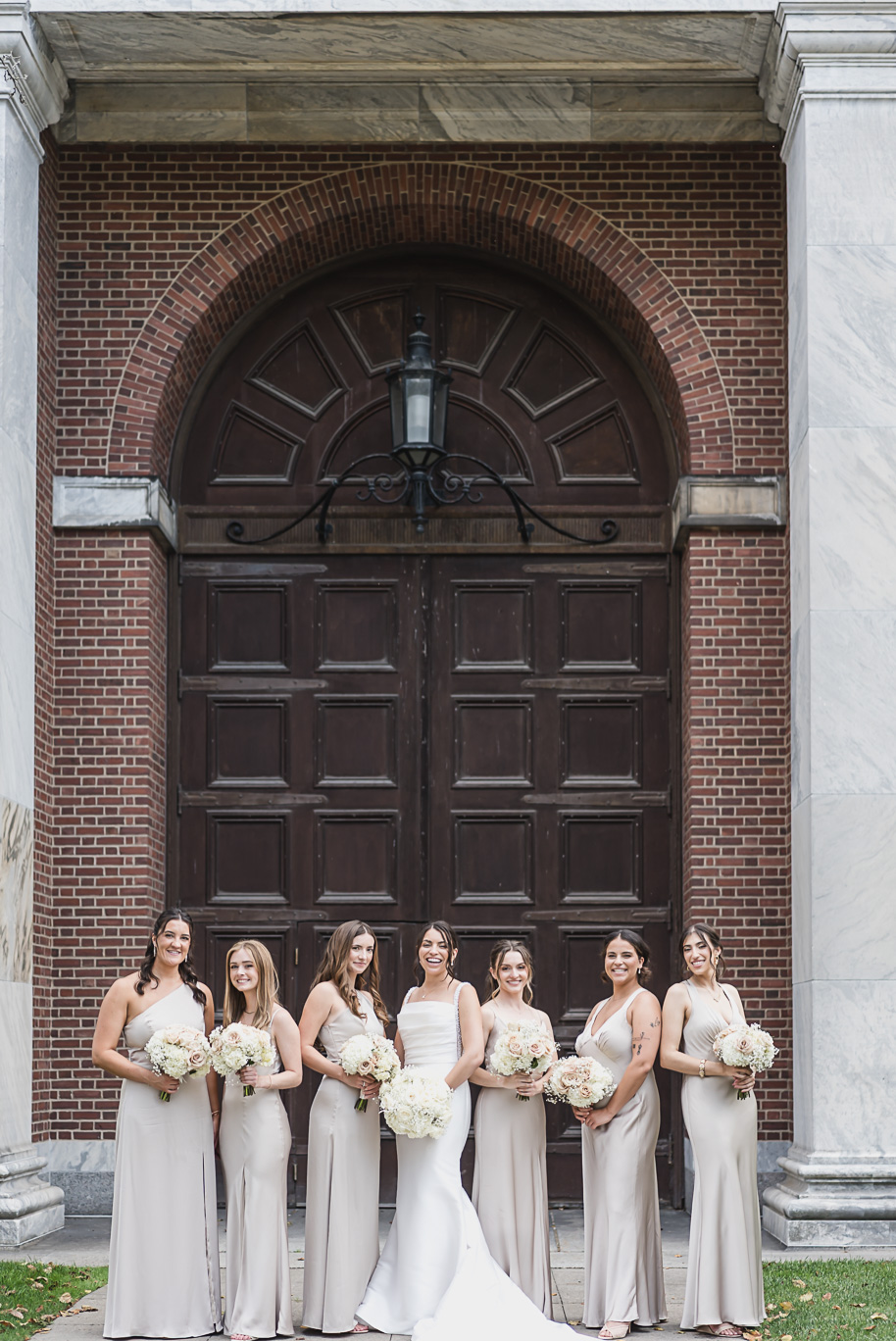 Bride and groom stand with their wedding party outside Lovett Hall, groomsmen in black tuxedos and bridesmaids in champagne gowns.