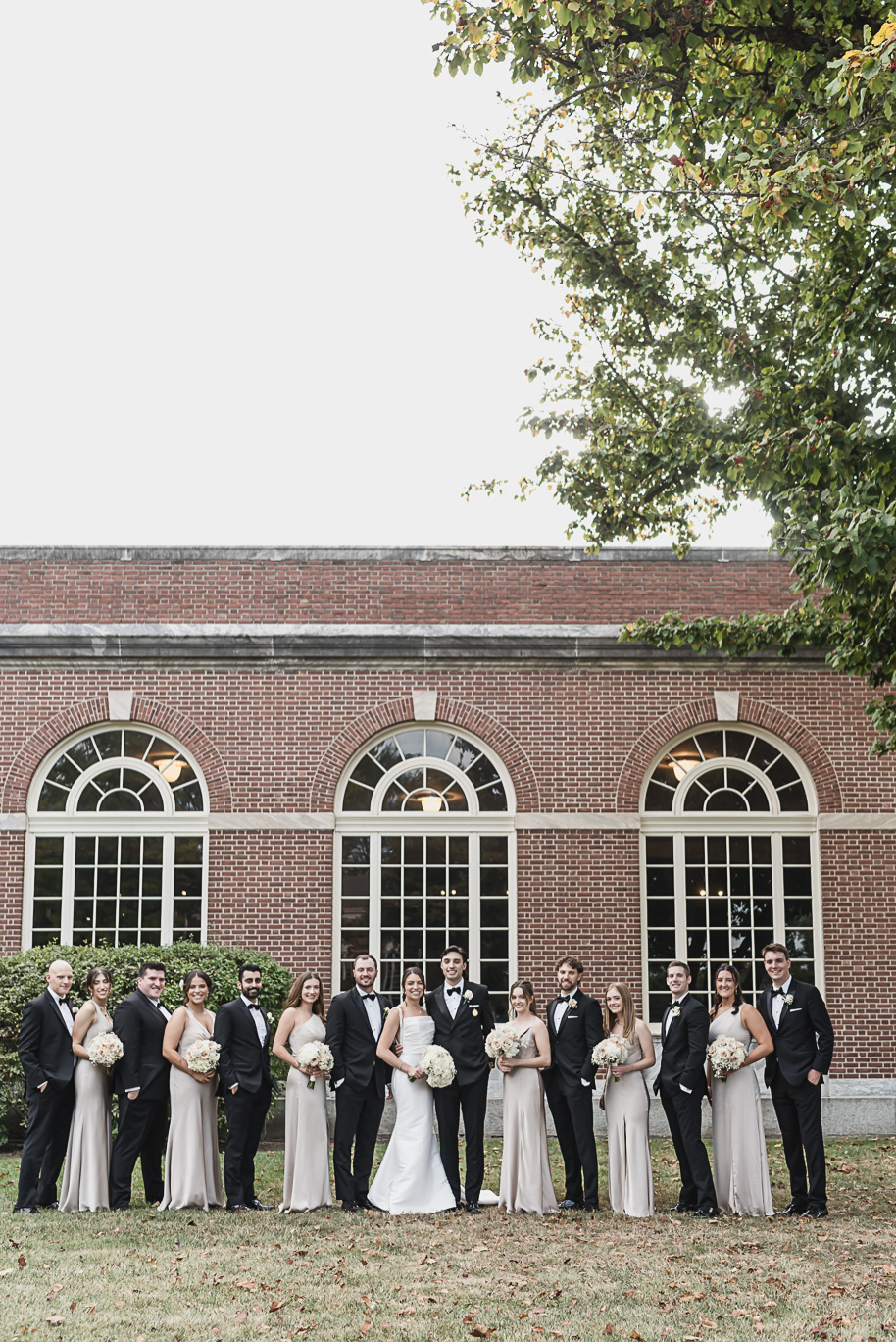 Bride and groom stand with their wedding party outside Lovett Hall, groomsmen in black tuxedos and bridesmaids in champagne gowns.