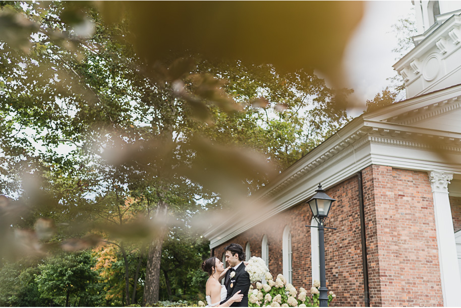 Newlyweds pose with their vintage ivory getaway car at night outside Lovett Hall, glowing with romantic lights.

