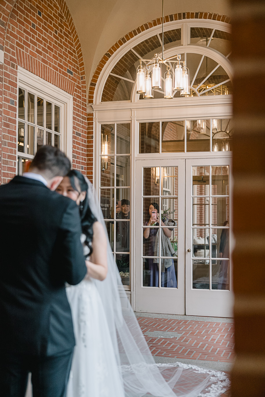 The bride's mom and bridesmaids look on through the windows of the Dearborn Inn during the first look between the bride and groom.